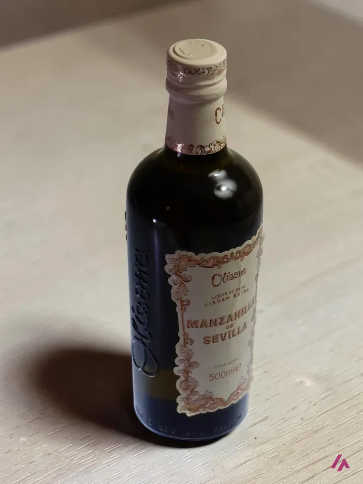 Foto final descargada de Photoroom: botella de aceite de oliva virgen extra de Sevilla sobre una encimera de madera clara con su sombra